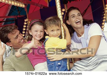 Stock Image - Young couple sitting on a carousel with their son and daughter. Fotosearch