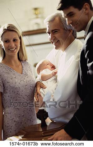 Stock Image - Young couple standing with a priest carrying their baby. Fotosearch
