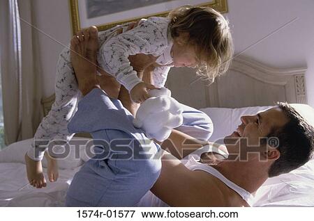 Stock Photo - Young man playing with his daughter on the bed. Fotosearch