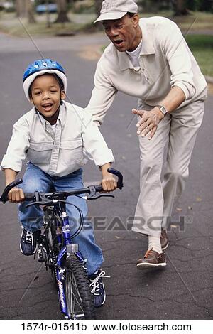 Stock Image - Young man teaching his son to ride a bicycle. Fotosearch
