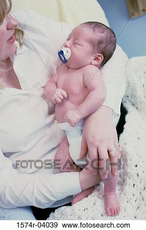 Stock Photo - Close-up of a baby boy sucking on a pacifier sleeping in his mother's arms. Fotosearch