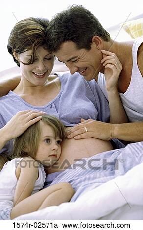 Stock Image - Daughter with her head against her pregnant mother's abdomen. Fotosearch