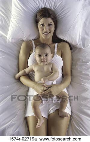 Stock Image - High angle view of a mother lying on a bed with her baby boy. Fotosearch