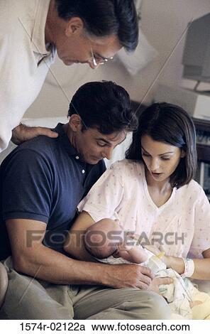 Stock Image - Parent carrying their baby boy with a senior man standing beside them. Fotosearch
