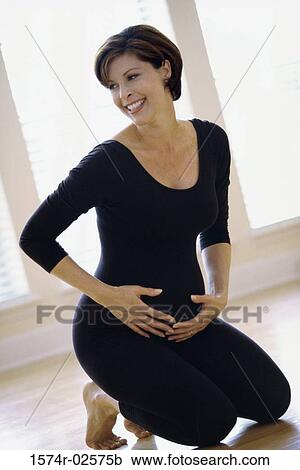 Stock Image - Portrait of a pregnant woman touching her abdomen. Fotosearch