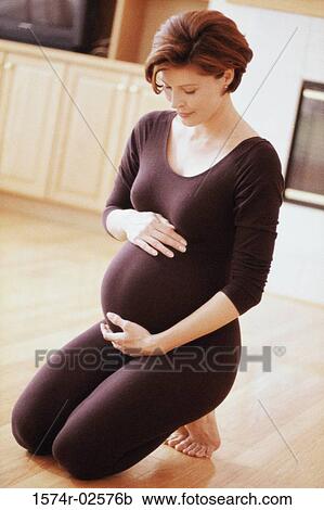 Pregnant woman kneeling on the floor touching her abdomen View Large Photo Image Stock Image - Pregnant woman kneeling on the floor touching her abdomen. Fotosearch