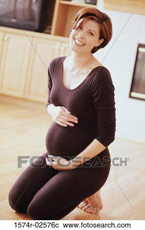 Stock Image - Pregnant woman kneeling on the floor touching her abdomen. Fotosearch