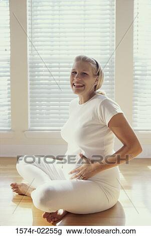 Stock Image - Pregnant woman sitting on the floor touching her abdomen. Fotosearch