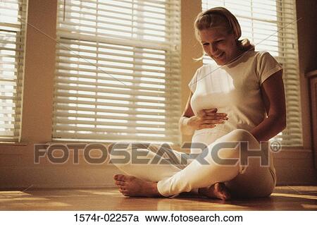 Pregnant woman sitting on the floor touching her abdomen View Large Photo Image Stock Image - Pregnant woman sitting on the floor touching her abdomen. Fotosearch
