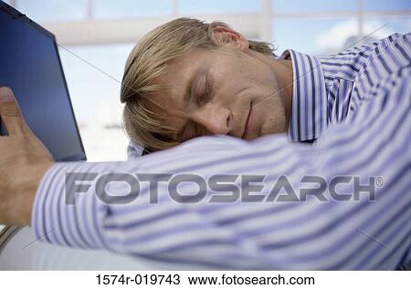 Close-up of a businessman sleeping on a table in front of a laptop View Large Photo Image Stock Image - Close-up of a businessman sleeping on a table in front of a laptop. Fotosearch