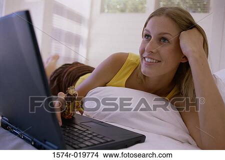 Close-up of a young woman lying on the bed and using a laptop View Large Photo Image Picture - Close-up of a young woman lying on the bed and using a laptop. Fotosearch
