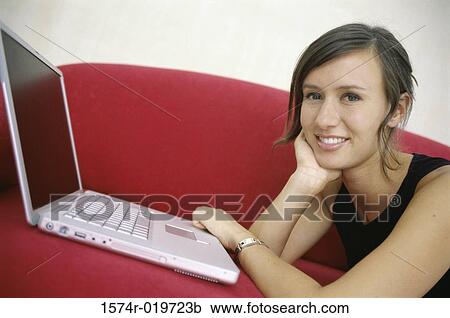 Portrait of a young woman lying on a couch in front of a laptop View Large Photo Image Stock Image - Portrait of a young woman lying on a couch in front of a laptop. Fotosearch