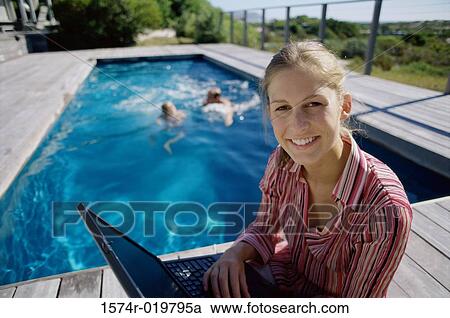 Portrait of a young woman sitting at poolside and using a laptop View Large Photo Image Stock Image - Portrait of a young woman sitting at poolside and using a laptop. Fotosearch