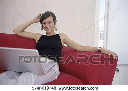 Stock Photo - Young woman sitting on a couch with a laptop on her lap. Fotosearch