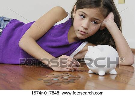 Stock Photo - Close-up of a girl lying on the floor looking at a piggy bank. Fotosearch