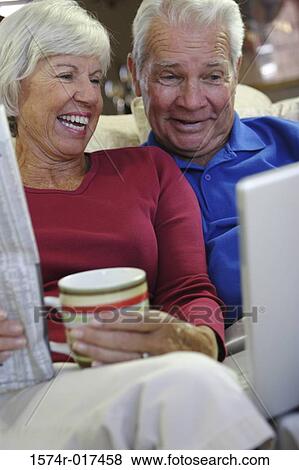 Stock Photo - Close-up of a senior couple sitting on a couch looking at a laptop. Fotosearch