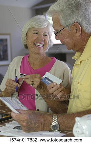 Stock Image - Close-up of a senior woman cutting a credit card with a pair of scissors. Fotosearch