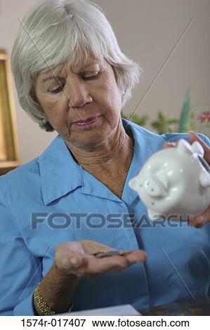 Stock Photo - Close-up of a senior woman holding a piggy bank and coins. Fotosearch
