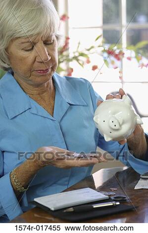 Stock Photography - Close-up of a senior woman holding a piggy bank and coins. Fotosearch