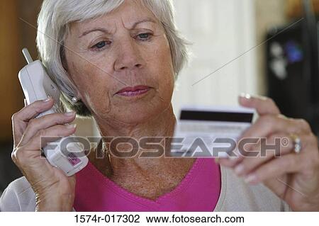 Stock Image - Close-up of a senior woman using a cordless phone holding a credit card. Fotosearch