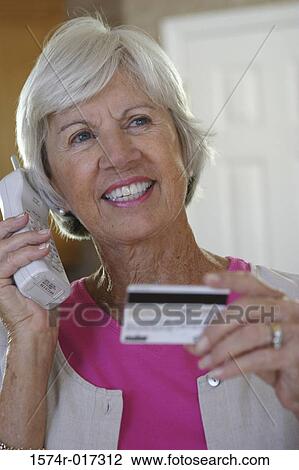 Stock Image - Close-up of a senior woman using a cordless phone holding a credit card. Fotosearch