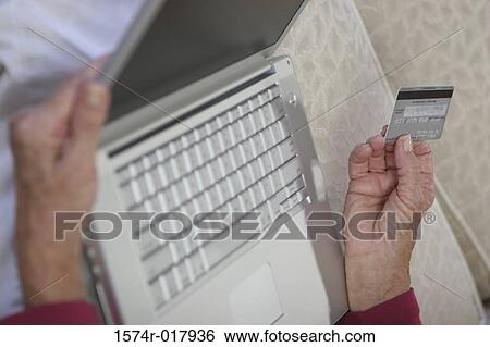 Stock Photograph - Close-up of a woman's hands holding a credit card and a laptop. Fotosearch