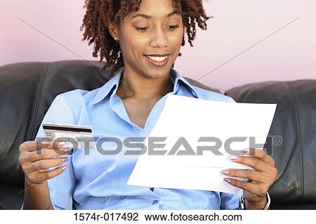 Close-up of a young woman holding a credit card reading a bill View Large Photo Image Stock Image - Close-up of a young woman holding a credit card reading a bill. Fotosearch