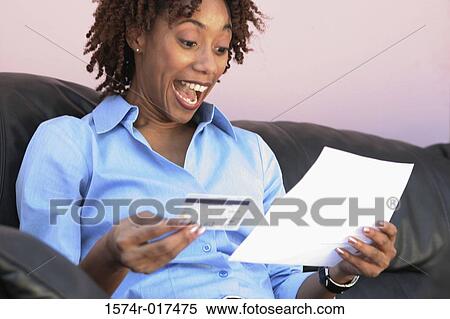 Stock Photography - Close-up of a young woman holding a credit card and a bill. Fotosearch