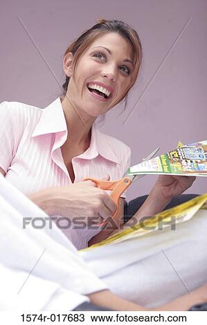 Stock Image - Low angle view of a young woman cutting paper and smiling. Fotosearch