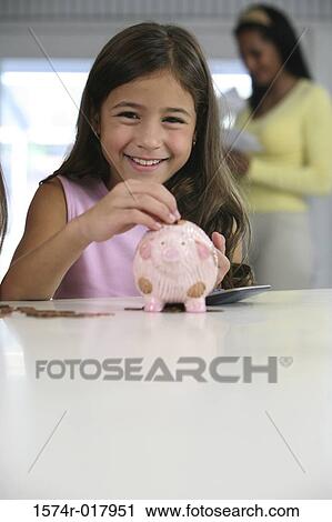 Stock Image - Portrait of a girl inserting coins into a piggy bank. Fotosearch