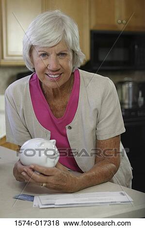 Portrait of a senior woman holding a piggy bank smiling View Large Photo Image Stock Photo - Portrait of a senior woman holding a piggy bank smiling. Fotosearch