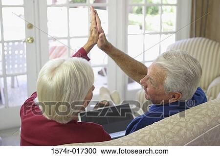 Rear view of a senior couple sitting on a couch and giving a high five to each other View Large Photo Image Stock Image - Rear view of a senior couple sitting on a couch and giving a high five to each other. Fotosearch