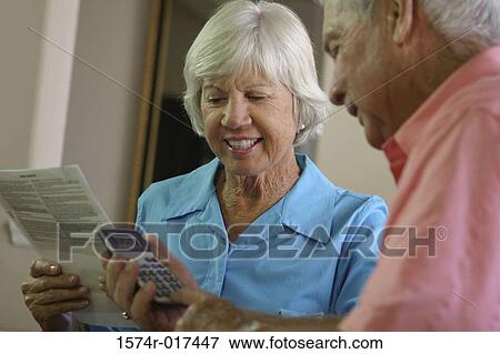 Senior man using a calculator with a senior woman sitting beside him View Large Photo Image Stock Photo - Senior man using a calculator with a senior woman sitting beside him. Fotosearch