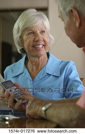 Stock Photograph - Senior man using a calculator with a senior woman sitting beside him. Fotosearch