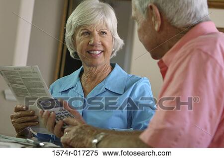 Senior man using a calculator with a senior woman sitting beside him View Large Photo Image Stock Photography - Senior man using a calculator with a senior woman sitting beside him. Fotosearch