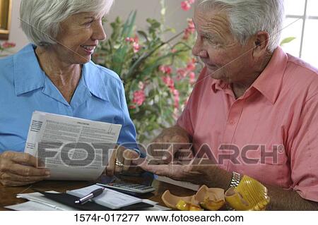 Senior woman holding a bill looking at a senior man View Large Photo Image Stock Photo - Senior woman holding a bill looking at a senior man. Fotosearch