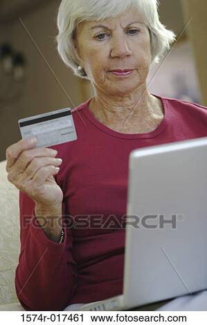 Senior woman sitting in front of a laptop holding a credit card View Large Photo Image Stock Image - Senior woman sitting in front of a laptop holding a credit card. Fotosearch