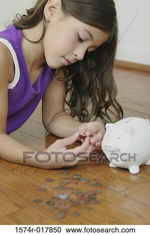Stock Image - Side profile of a girl lying on the floor counting coins. Fotosearch