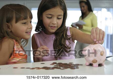 Stock Image - Two sisters looking at a piggy bank with their mother standing in the background. Fotosearch