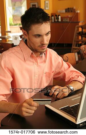 Young man sitting using a laptop holding a credit card View Large Photo Image Stock Photograph - Young man sitting using a laptop holding a credit card. Fotosearch