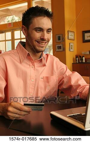 Young man sitting using a laptop holding a credit card View Large Photo Image Stock Photography - Young man sitting using a laptop holding a credit card. Fotosearch