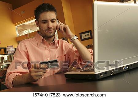Stock Image - Young man talking on a mobile phone holding a credit card. Fotosearch