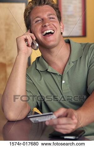 Young man talking on a mobile phone holding a credit card View Large Photo Image Stock Image - Young man talking on a mobile phone holding a credit card. Fotosearch