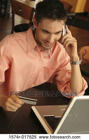 Young man talking on a mobile phone holding a credit card View Large Photo Image Stock Photography - Young man talking on a mobile phone holding a credit card. Fotosearch