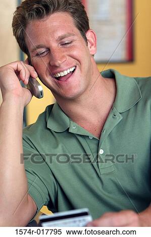 Stock Photography - Young man talking on a mobile phone holding a credit card. Fotosearch