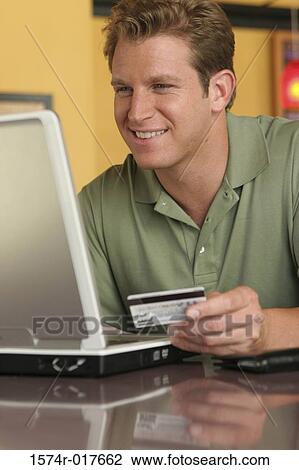 Young man using a laptop holding a credit card View Large Photo Image Stock Image - Young man using a laptop holding a credit card. Fotosearch