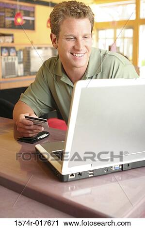 Young man using a laptop holding a credit card View Large Photo Image Stock Image - Young man using a laptop holding a credit card. Fotosearch