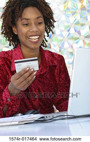 Young woman sitting in front of a laptop holding a credit card View Large Photo Image Picture - Young woman sitting in front of a laptop holding a credit card. Fotosearch