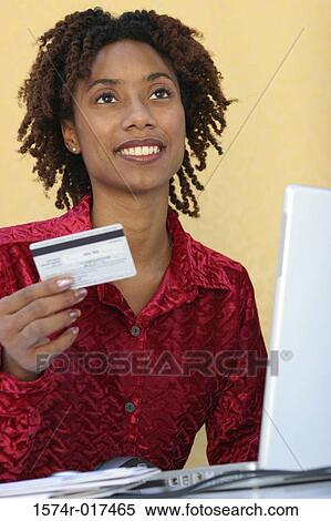 Young woman sitting in front of a laptop holding a credit card View Large Photo Image Stock Photography - Young woman sitting in front of a laptop holding a credit card. Fotosearch