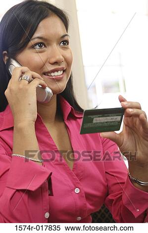 Stock Photography - Young woman talking on a mobile phone holding a credit card. Fotosearch